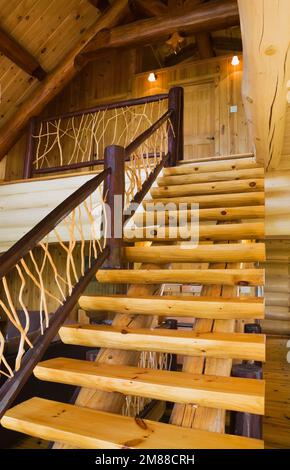 Treppen aus weißem Kiefernholz mit Zedernholzgeländern, die zum oberen Stockwerk in einem Blockhaus im skandinavischen Stil führen. Stockfoto