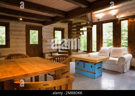 Hölzerner Frühstückstisch mit runden Stühlen im Wohnzimmer mit blauem Kaffeetisch, weiß gepolstertem Zweisitzersofa und braunen Flecktreppen. Stockfoto