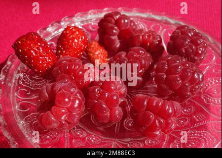 Frische Himbeeren und Erdbeeren Früchte gesunde Snacks. Ein Haufen roter Beeren auf einer verzierten Glasuntertasse auf einem magentafarbenen Tuch Stockfoto