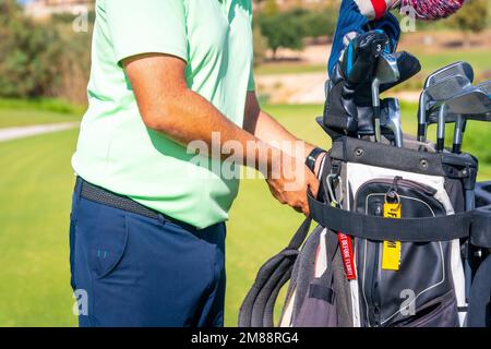 Ein Mann, der Golf spielt, die Schlägertasche aufhebt und sie in den Buggy legt Stockfoto