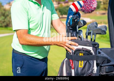 Ein Mann, der Golf spielt, die Schlägertasche aufhebt und sie in den Buggy legt Stockfoto