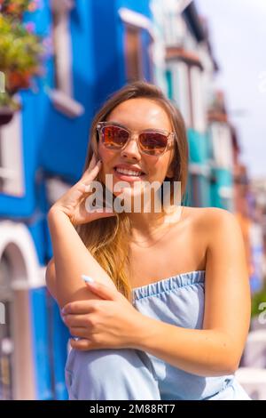 Porträt einer attraktiven jungen blonden Frau mit Sonnenbrille in einer posierten, blauen, bunten Fassade Stockfoto