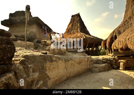 Ein megalithisches Grab und Vernamenshäuser mit Strohdächern in der indigenen Siedlung Praijing in Tebara, Waikabubak, West Sumba, Nusa Tenggara, Indonesien. „Die Sumbanesen bauen ein traditionelles Haus aus Materialien, die der Natur entnommen wurden, denn es wurde in unserem Glauben an Marapu gesagt: Wir müssen in einer Linie mit der Natur leben“, sagte Umbu Tiu, ein Dorfbewohner. Bei der Antizipierung der Auswirkungen des Klimawandels "müssen wir lokalen, ortsbasierten indigenen Kenntnissen den nötigen Respekt zollen", sagt Karim-Aly S. Kassam, internationaler Professor für Umwelt- und indigene Studien. Stockfoto