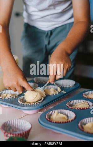 Familie kocht Muffins zusammen in der Küche, Junge gießt rohen Teig in Silikonformen. Muttertag, Familie, hausgemachtes Backen gesundes Essen Stockfoto