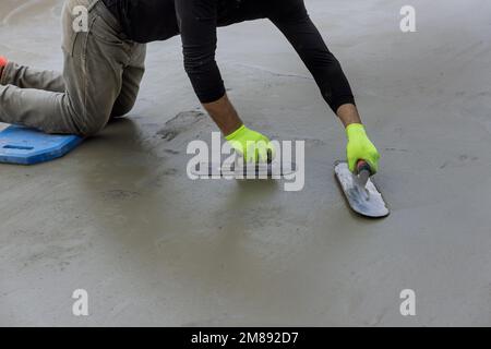 Beim Verputzen von Beton auf Zementboden hält der Arbeiter eine Stahlkelle in der Hand, während er den Beton glättet Stockfoto