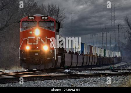 Elgin, Illinois, USA. Mit einem Labyrinth aus Stromleitungen und Türmen im Hintergrund treibt eine Lokomotive der Canadian National Railway eine intermodale Fracht an. Stockfoto