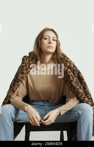 Studiofoto eines jungen weiblichen Models, das blaue Jeans, ein beigefarbenes Hemd und einen Leopardenteddy-Mantel trägt. Stockfoto