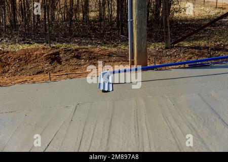 Im Baubereich hält der Arbeiter eine fresno-Kelle aus Stahl und glättet neue Gehwege auf nassem Beton aus frisch gegossenem Gehweg Stockfoto