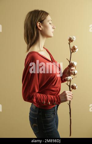 Studiofoto eines jungen weiblichen Models im Hemd aus biologischer Baumwolle mit Baumwollblumen. Konzept von komfortabler und nachhaltiger Mode. Stockfoto