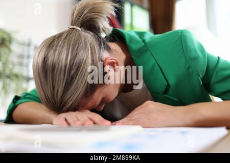 Erschöpfte und müde Frau, die im Büro auf ihrem Schreibtisch schläft. Stockfoto
