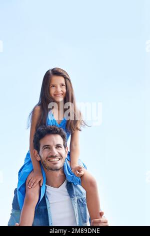 Wenn ich bei Daddy bin, bin ich auf der Spitze der Welt. Ein kleines Mädchen, das auf den Schultern des Vaters sitzt, gegen den blauen Himmel. Stockfoto