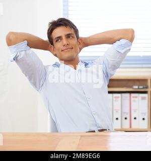 Er träumt sein nächstes Vorhaben. Ein selbstbewusster junger Geschäftsmann lehnt sich mit den Händen hinter dem Kopf zurück in seinen Stuhl. Stockfoto