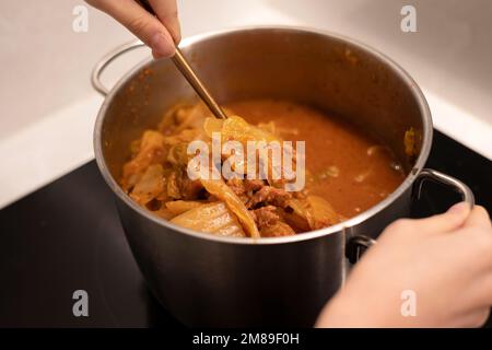 Kochen Sie Kimchi-Eintopf mit einem Topf, rühren Sie den scharfen Eintopf mit einem Löffel um Stockfoto