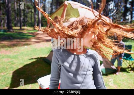 Camping macht Spaß. Ein junges, rotes Mädchen, das sich auf einem Campingplatz die Haare dreht. Stockfoto