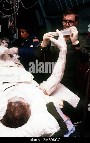 MAJ. Bard, Mitglied der 2. Aeromedizinischen Evakuierungsschwadron, und MAJ Gilliam, Mitglied des Wiesbaden Krankenhauspersonals, wechseln die Kleidung für PETTY Officer 3. Klasse David Burbine. Der Seemann, der an Bord eines 438. Militärflugzeugs Win g C-141B Starlifter zur weiteren Behandlung nach Deutschland transportiert wird, war einer von vier Besatzungsmitgliedern, die schwer verletzt wurden, als die Führungsraketenfregatte USS SAMUEL B. ROBERTS (FFG-58) während des Betriebs im Persischen Golf eine Mine traf. Land: Unbekannt Stockfoto