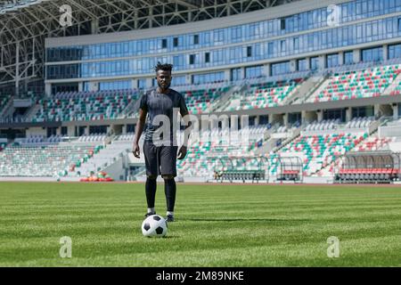 Ein afroamerikanischer Mann, der Fußball auf dem Stadion spielt. Ein Mann läuft mit einem Fußball über das Spielfeld. Stockfoto