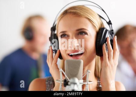 Süßer singvogel. Eine junge blonde Frau, die in ein Mikrofon singt, mit ihren Bandmitgliedern im Hintergrund. Stockfoto