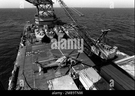 Der Kran an an Bord des Kutschers Hercules bereitet sich darauf vor, ein Patrouillenboot PB Mark III für eine Patrouille ins Wasser zu heben. Die 65 Meter langen Patrouillenboote aus Aluminium arbeiten paarweise, um die Aktivität kleiner Boote im Golf zu überwachen. Ein speziell ausgerüsteter US-amerikanischer Der Army UH-60 Black Hawk (Blackhawk) Helikopter ist auf dem Hubschrauberlandeplatz geparkt. Land: Unbekannt Stockfoto