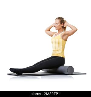 Sie nimmt ihre Fitness ernst. Eine junge Frau, die auf einer Schaumstoffwalze sitzt, mit erhobenen Armen, um ihren Kern zu stärken. Stockfoto