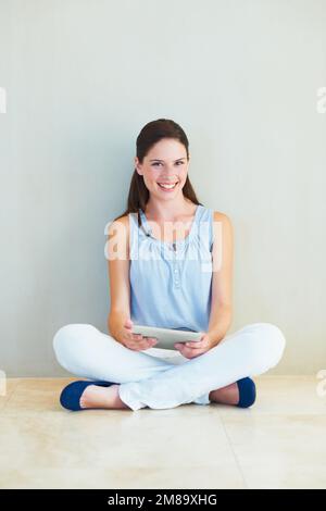 Bloggen mit ihrem Tablet. Eine schöne junge Frau, die auf dem Boden sitzt und an ihrem Tablet arbeitet. Stockfoto
