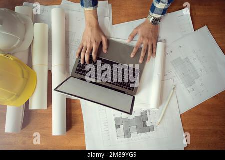 Architekt, der mit Laptop und Bauplänen arbeitet, Ingenieur am Arbeitsplatz auf Architekturplan überprüft, Skizze des Bauprojekts. Stockfoto