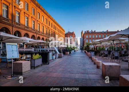 Stühle, Tische und Sonnenschirme einer Café-Terrasse auf dem Capitole-Platz in Toulouse im Süden Frankreichs (Haute Garonne) Stockfoto