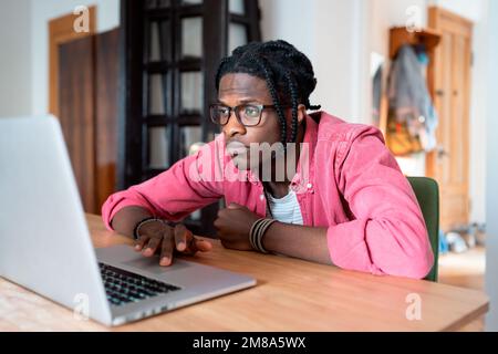 Trauriger afrikanischer Außendienstmitarbeiter, der sich unmotiviert fühlt, während er ein langweiliges freiberufliches Projekt durchführt Stockfoto