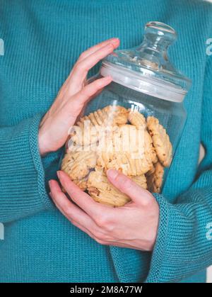 Glasbehälter mit hausgemachten Keksen in menschlichen Händen, selektiver Fokus. Kekse im vertikalen Format Stockfoto