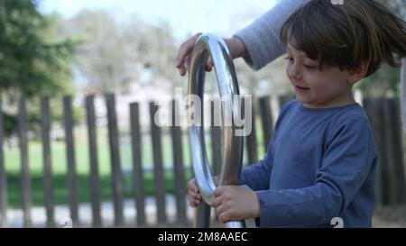 Das Kind dreht sich auf dem Spielplatz. Ein kleiner Junge, der mit einem Edelstahlspielzeug Spaß am Spielplatz hat Stockfoto