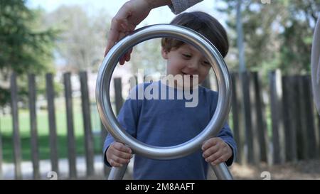 Das Kind dreht sich auf dem Spielplatz. Ein kleiner Junge, der mit einem Edelstahlspielzeug Spaß am Spielplatz hat Stockfoto