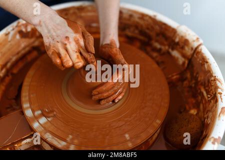 Zugeschnittenes Bild eines nicht wiedererkennbaren weiblichen Keramikmachers, das mit dem Keramikrad in Cozy Workshop arbeitet, macht eine Vase oder Tasse der Zukunft, kreatives Handwerk für Menschen Stockfoto