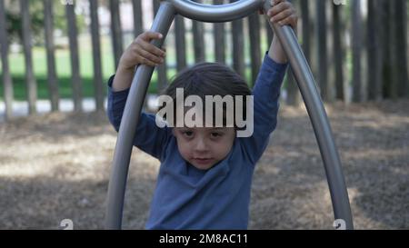 Das Kind dreht sich auf dem Spielplatz. Ein kleiner Junge, der mit einem Edelstahlspielzeug Spaß am Spielplatz hat Stockfoto