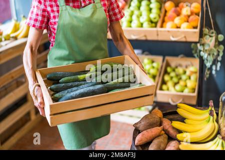 Arbeiter im Obst- und Gemüseladen ist Korb mit Gurke. Stockfoto