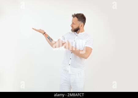 Sportlicher bärtiger Mann mittleren Alters im Stehen, mit offener Handfläche die Hand heben, mit Zeigefinger auf weißen Hintergrund zeigen. Stockfoto