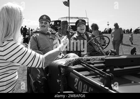 Zwei Männer in 1940er-Uniform und ein Jeep aus dem Krieg lachen, während sie mit einer Frau während eines Festivals in Lytham, Lancashire, im Jahr 2022 sprechen. Stockfoto