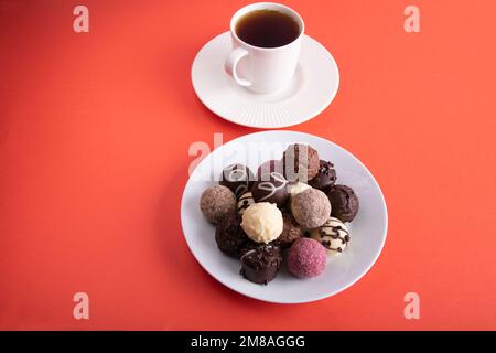 Fotografieren Sie mehrfarbige Süßigkeiten auf einem weißen runden Teller neben einer Tasse mit einem heißen Getränk Stockfoto