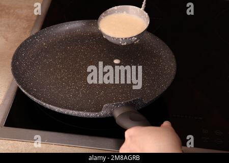 Foto in einer Schüssel Teig für dünne Pfannkuchen am Boden der Pfannkuchenpfanne Stockfoto