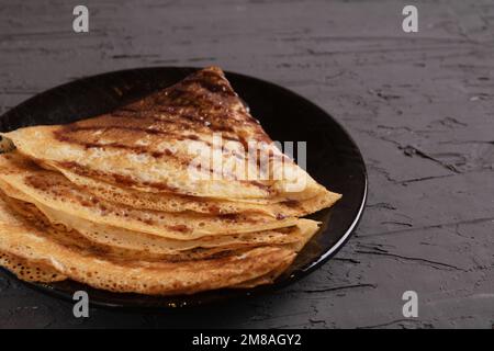 Dreieckige Pfannkuchen mit Fotoöffnungen und Sirup auf einem Teller auf dunklem Hintergrund Stockfoto