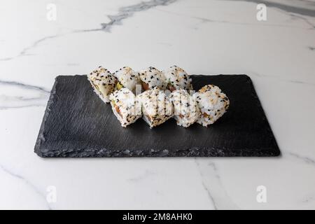 Ein Set kalifornischer Brötchen in Sesamsamen, serviert auf dem schwarzen Brett auf dem Marmortisch Stockfoto