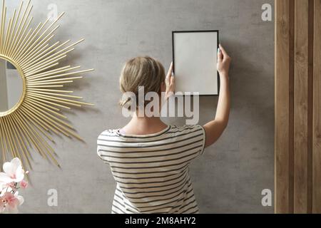 Frau, die Bilderrahmen an der Wand in einem neuen Haus anlegt, heimwerkerkonzept Stockfoto