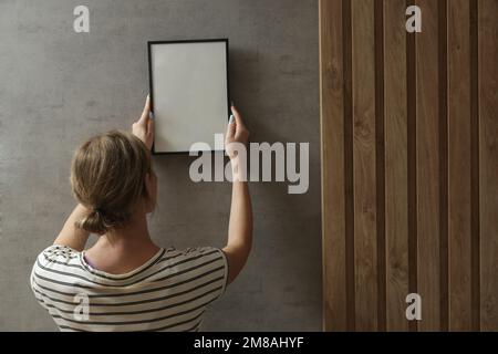 Frau, die Bilderrahmen an der Wand in einem neuen Haus anlegt, heimwerkerkonzept Stockfoto