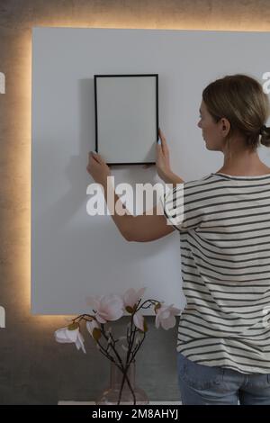 Frau, die Bilderrahmen an der Wand in einem neuen Haus anlegt, heimwerkerkonzept Stockfoto