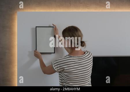 Frau, die Bilderrahmen an der Wand in einem neuen Haus anlegt, heimwerkerkonzept Stockfoto