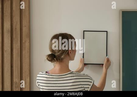 Frau, die Bilderrahmen an der Wand in einem neuen Haus anlegt, heimwerkerkonzept Stockfoto