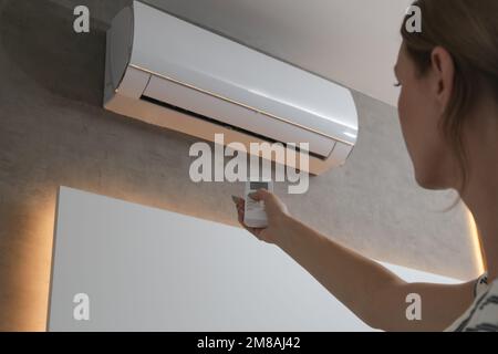 Junge Frau stellt Klimaanlage mit Fernbedienung ein Stockfoto