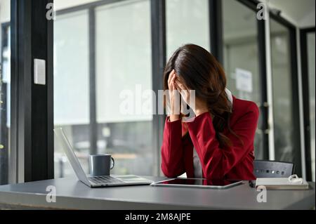 Gestresste und depressive asiatische Geschäftsfrau der Millennials sitzt an ihrem Schreibtisch und macht sich Sorgen um ihr Projekt. Stockfoto