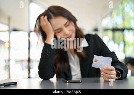Selektive Fokussierung, gestresste und unglückliche junge asiatische Geschäftsfrau oder Büroangestellte mit einer Kreditkarte am Schreibtisch, die finanzielle Probleme hat. Stockfoto