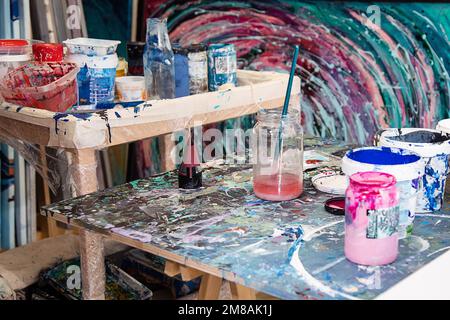 Interieur des Workshops für kreative Kunst. Verschiedene Eimer mit Farbe, schmutzige Glasgefäße, Holzschreibtische mit Farbe befleckt. Stockfoto