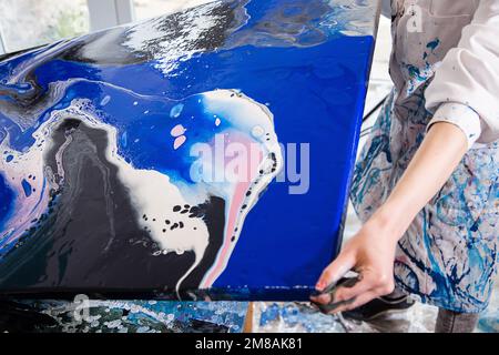 Zugeschnittenes Foto von Händen einer Frau, die ein weißes Hemd trägt, mit Flecken bedeckter Bademantel mit Leinwand und abstraktem Bild. Stockfoto
