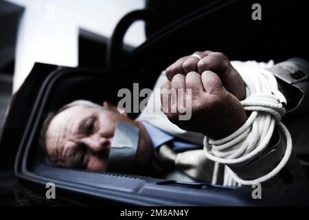 Es gibt kein Entkommen. Ein ängstlicher Geschäftsmann, gefesselt und geknebelt im Kofferraum seines Autos. Stockfoto
